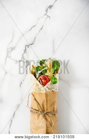 Fresh tortilla wrap on a marble pattern tabletop tied round with brown paper and string. Top view shot. Gourmet conception.