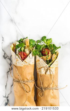 Fresh tortilla wraps on a marble pattern tabletop tied round with brown paper and string. Top view shot. Gourmet conception.
