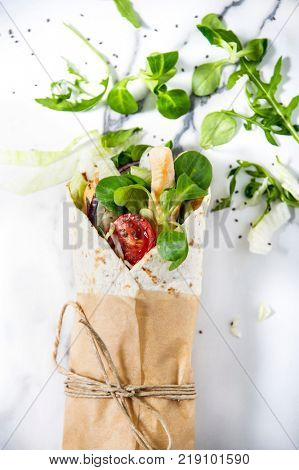 Fresh tortilla wrap  with vegetables and chicken. Tied round with brown paper and string. Marble tabletop. Top view shot.