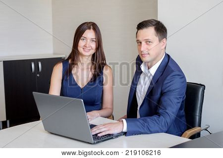 Business man explaining something to a woman with a laptop in an office.