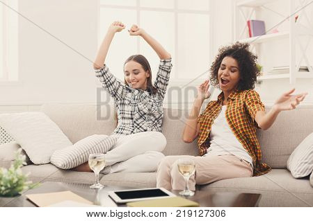 Happy female friends chatting and drinking wine at home. Two young women having friendly talk, gossiping and celebrating new life, slumber party, copy space
