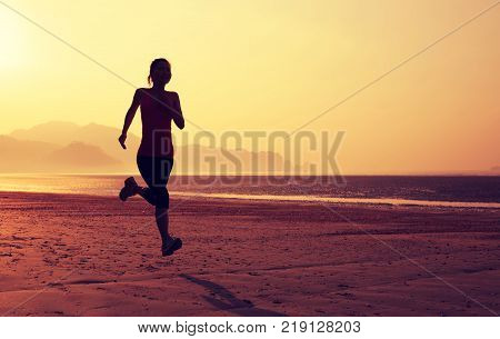 Young fitness woman running on sunrise sandy beach