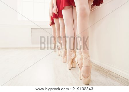 Ballet background, young ballerinas training. Female dancers legs in pointe shoes, making exercises. Classical dance school, copy space, crop
