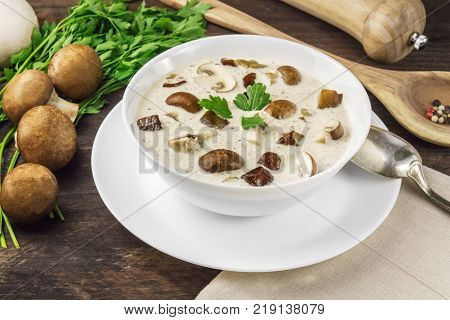 A photo of a plate of a mushroom cream soup with champignons, cremini, fresh parsley, and pepper, on a dark rustic background texture with a place for text