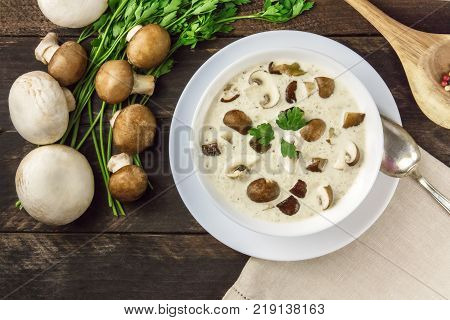 An overhead photo of a plate of a mushroom cream soup with champignons, cremini, fresh parsley, on a dark rustic background texture with a place for text