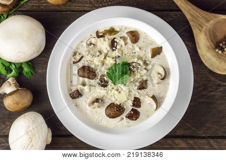 An overhead closeup photo of a plate of a mushroom cream soup with champignons, cremini, fresh parsley, on a dark rustic background texture