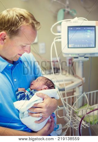 Smiling father holding his newborn baby son in a hospital room