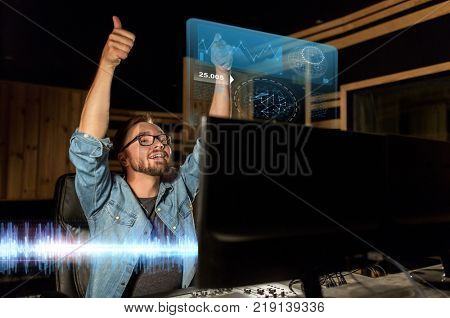 music, technology, gesture and people concept - happy man at mixing console in sound recording studio showing thumbs up