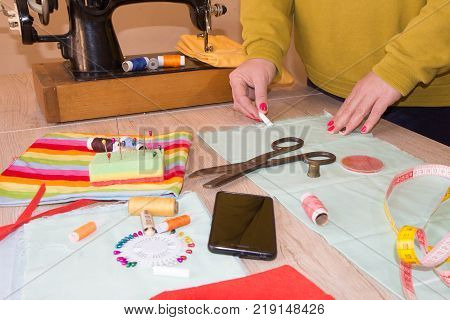 Woman dressmaker drawing tailor pattern with chalk for a clothing on the table. The outline on the fabric painted chalk. Garment industry tailoring concept