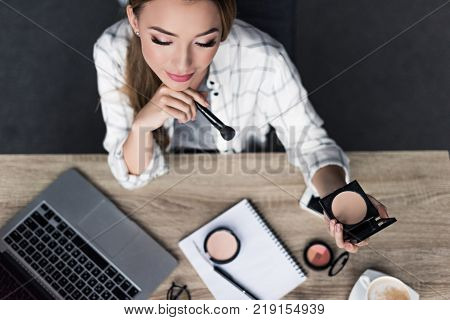 top view of thoughtful young woman doing makeup at workplace