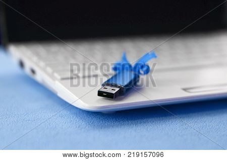 Brilliant blue usb flash memory card with a blue bow lies on a blanket of soft and furry light blue fleece fabric beside to a white laptop. Classic female gift design for a memory card