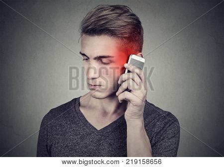 Man on the cellphone with headache. Upset unhappy guy talking on a phone isolated on gray wall background. Negative human emotion face expression feeling reaction.