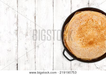 Crepes in a cast iron pan on light wooden background top view
