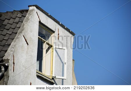 a old white dutch building roof with open shutters and a white framed glass window with a clear blue sky background.