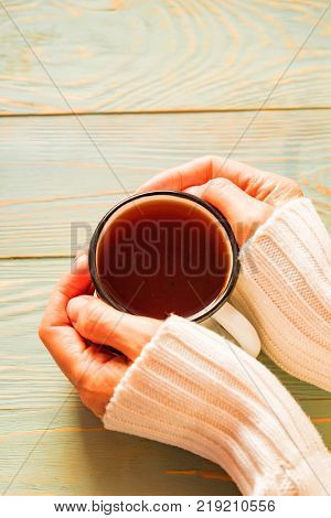 Woman's hands in sweater holding cup of tea over the wooden table. Cinnamon and cookies. Winter cosy atmosphere. Hygge concept