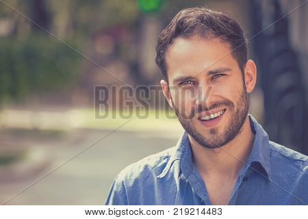 Happy young man. Closeup portrait of handsome guy in casual shirt smiling while standing against city urban background