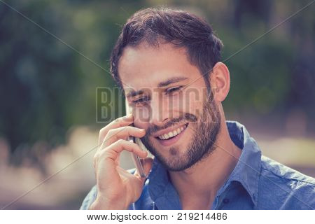 Headshot of a man talking on mobile phone. Casual urban professional using smartphone smiling happy standing outside on a street . Outdoor portrait of modern guy with cellphone