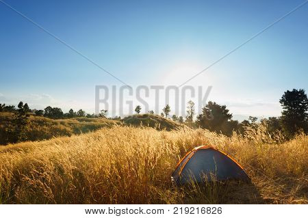outdoors camping grass highlands mountain in the Sunset.outdoors camping highlands mountain.Orange tent on a hill above the river. The concept of freedom and adventure. Sunlit meadow at dawn. Symbol of a new day.