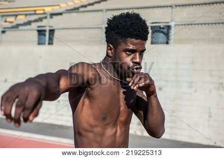 Muscular Jamaican boxer throwing right punch while shadowboxing on stadium track.