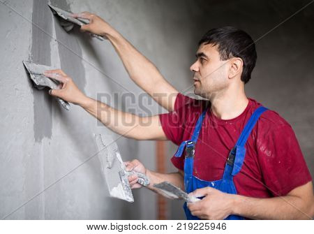 Collage worker with four hands makes repairs smears on wall putty