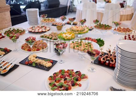 Close-up of a white restaurant buffet table, served with different delicios dishes like vegetable salads, canapees, shrimps appetizers and stuffed meat.