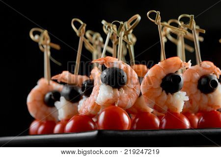Tasty restaurant appetizer with shrimps, tomatoes and black olives. Good cnack for alcohol, catering and buffet. Photo was made on the dark studio background