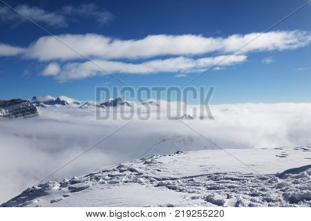 Snowy and sunlight mountains under clouds at nice sun day. Caucasus Mountains in winter Georgia region Gudauri. Viewpoint atop mount Kudebi.