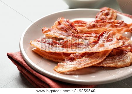 Plate with cooked bacon rashers on table, closeup