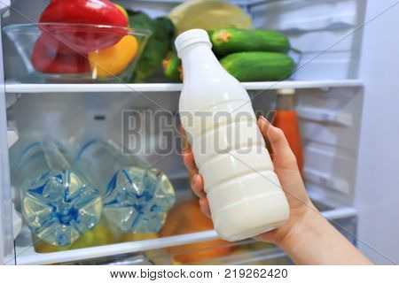 Woman taking bottle of milk from refrigerator, closeup