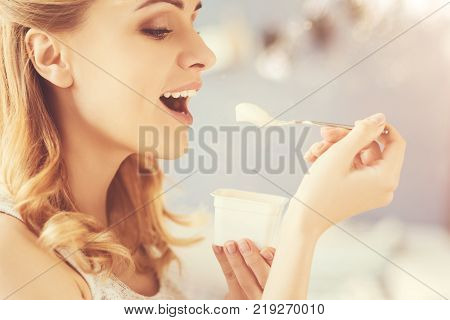 One more spoon. Positive delighetd woman eating joghurt and expressing joy while smiling