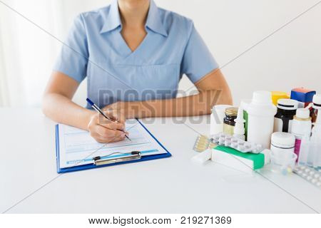 medicine, healthcare and people concept - nurse or doctor with drugs and clipboard writing prescription or medical report at hospital