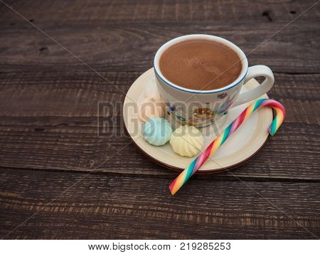 Freshly brewed cocoa and colorful biseza with candy on an old wooden table