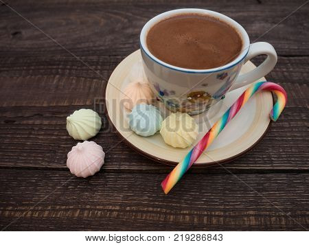 Freshly brewed cocoa and colorful biseza with candy on an old wooden table