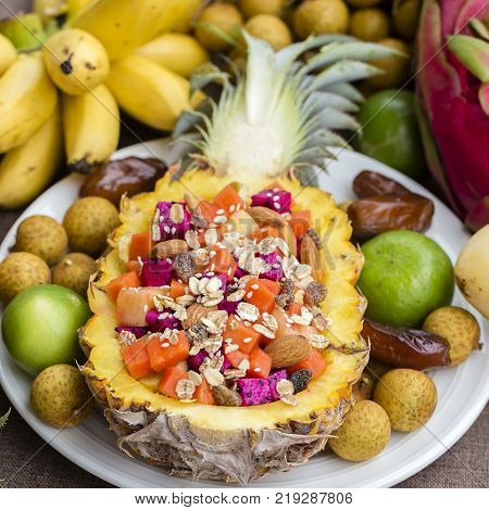 Fresh tropical fruit salad in pineapple with oat flakes raisins nuts sesame and mix sliced fruits ( dragon fruit pineapple banana mango papaya) - healthy breakfast. Thailand close up