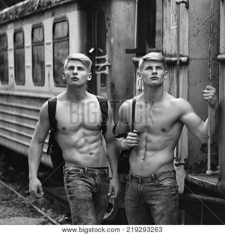 Handsome young guys with muscular body standing shirtless in pants with beautiful torso near blue old train railcar