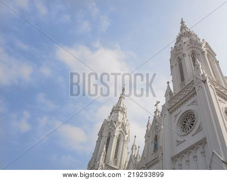The upper part of the Lourdes Cathedral of white color on the background with the blue sky. View of the Gothic style building in South India, Trichur
