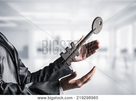 Business woman in black suit keeping big stone key in hands with office view on background. Mixed media.