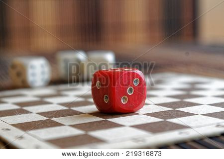 Stack of three white plastic dices and one red dice on brown wooden board background. Six sides cube with black dots. Number 3 2