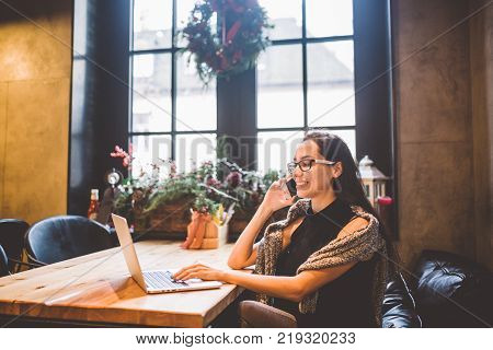 Beautiful Young Brunette Woman Inside Cafe With Christmas Interior At Wooden Table By The Window Tal