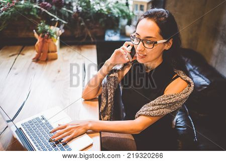 Beautiful Young Brunette Woman Inside Cafe With Christmas Interior At Wooden Table By The Window Tal