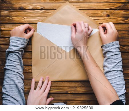 Mom and daughter open a large brown envelope and take out a letter or a clean white sheet of paper. Wooden background.
