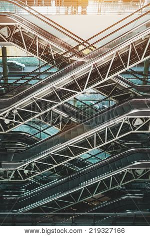 Side view of multiple criss-cross positioned empty modern escalators with visible internal mechanisms and gears located inside of contemporary airport terminal railway station or shopping mall