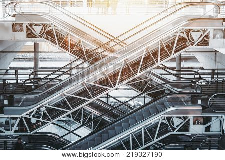 Side view of several criss-cross positioned empty modern escalators with opened internal mechanisms and gears in interior of contemporary airport terminal railway station or shopping mall on daytime