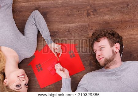 Home security safety future family mortgage finances concept. Young couple exchanging keys. Man and wona lying on floor with house cutout.
