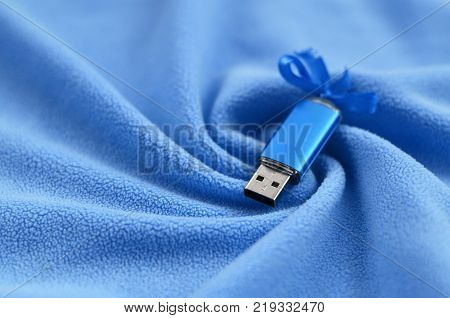 Brilliant blue usb flash memory card with a blue bow lies on a blanket of soft and furry light blue fleece fabric with a lot of relief folds. Memory storage device in women's design