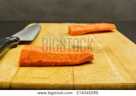 Peeled carrot root prepared for cutting on a chopping board.