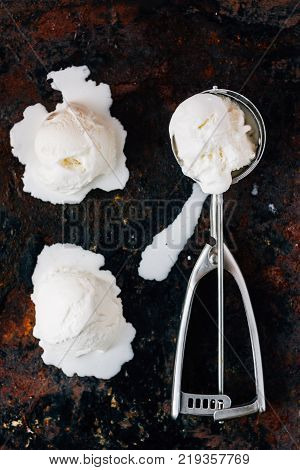 Melted ice cream in metal ice cream scooper over black rustic table