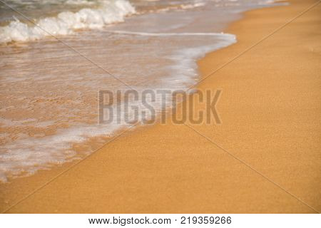 Background. A close up of a wave runs over a sandy beach