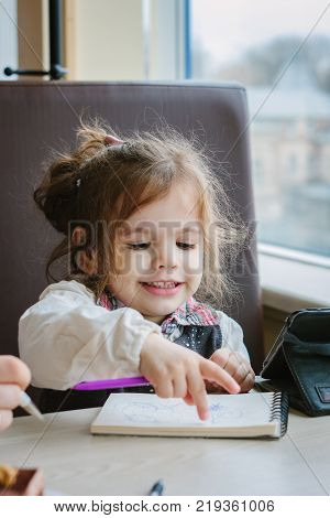 Little kid girl writing or drawing with pen in scetch book.