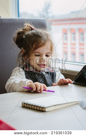 Little kid girl writing or drawing with pen in scetch book.